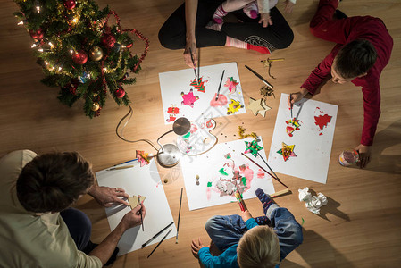 有孩子的年轻家庭在地板上环绕一棵Xmas树下跪做圣诞装饰图片