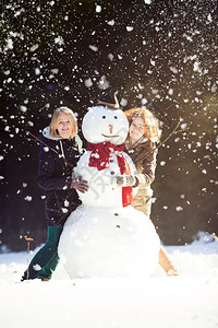 两个微笑的漂亮女孩与一个雪人一起在森林里冒着图片