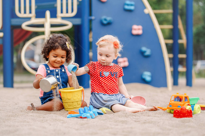 沙地两个可爱的白种人和西班牙裔拉丁婴儿坐在沙箱里玩塑料彩色玩具小女孩朋友们在操图片