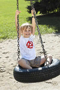 快乐的男孩在公园的轮胎秋千上荡秋千图片
