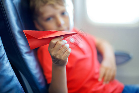 小男孩在飞机上飞行时玩红纸飞机孩子坐在窗边的飞机内一家人去度假选择图片