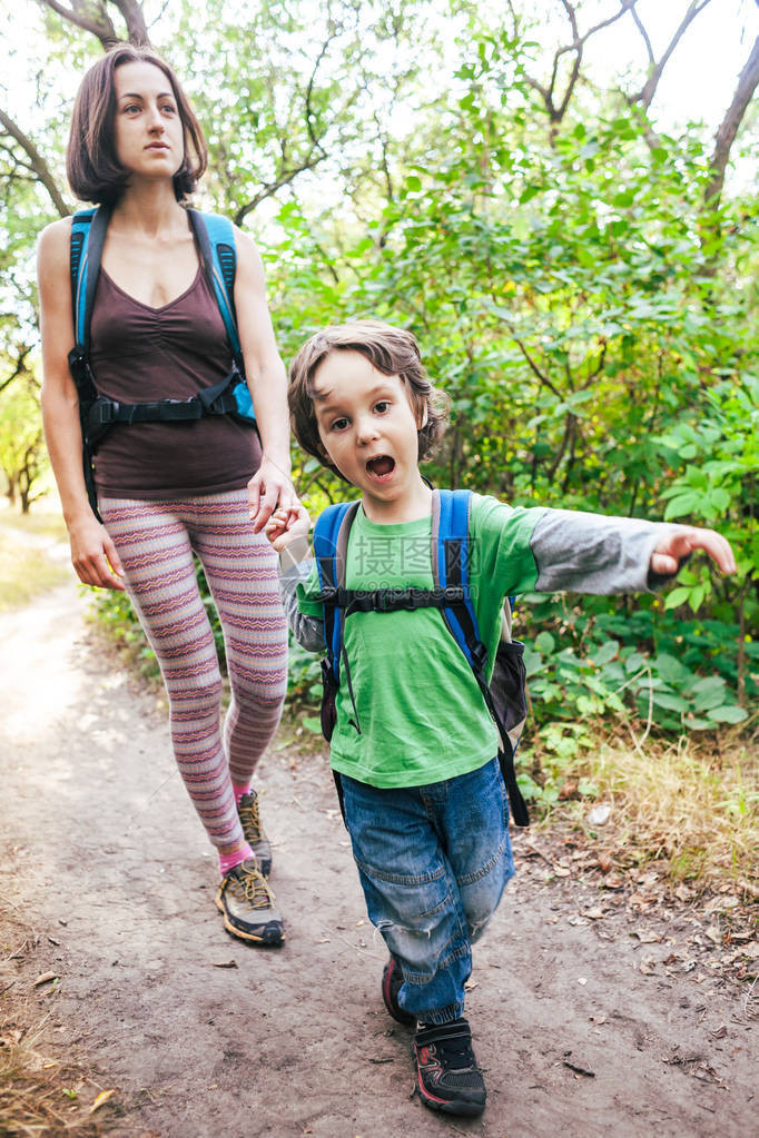 孩子在秋天向他的母亲展示了一条小径一家人在森林里徒步旅行带着孩子在秋天的公园里旅行一个女人和一个背着书包的孩子图片