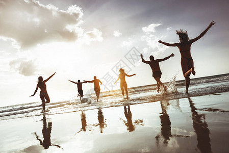 一群快乐的朋友在日落海滩奔跑跳跃图片