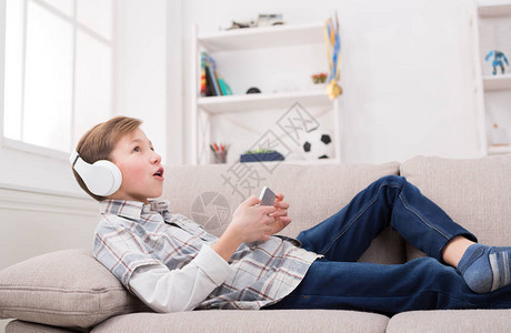 括号中的孩子从他的智能手机享受耳机中的音乐休闲的男孩躺在舒适的沙发图片