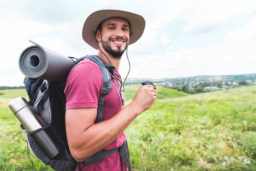 带着背包手持双目望远镜在草地上微笑的顶图片