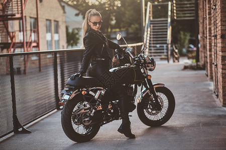 时髦的女摩托车手坐在她的黑色自行车上图片