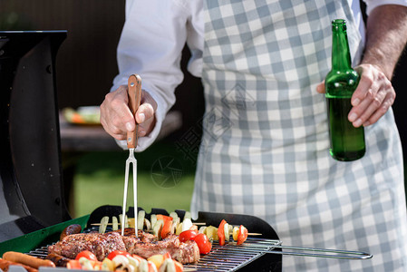 男子在烧烤上做肉和蔬菜用瓶装啤酒喝图片