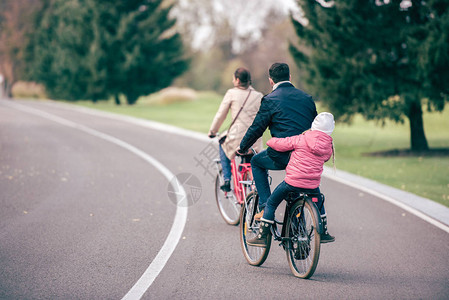 年轻家庭在秋季公园骑自行车的背影图片