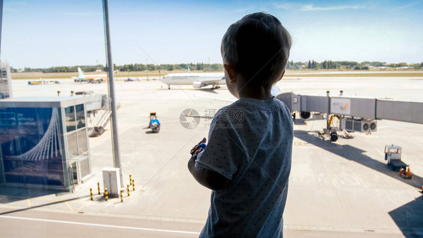 小孩男孩在机场大窗户上看着飞机图片