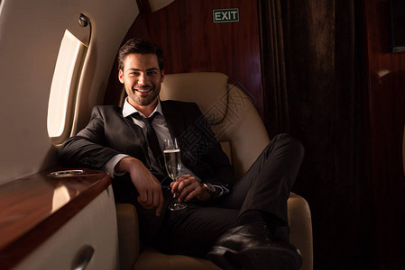 在飞机上拿着香槟杯子的英俊笑图片