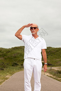 有胡子和太阳镜的退休老人在草地上漫步天空阴云茂密的草丘风图片