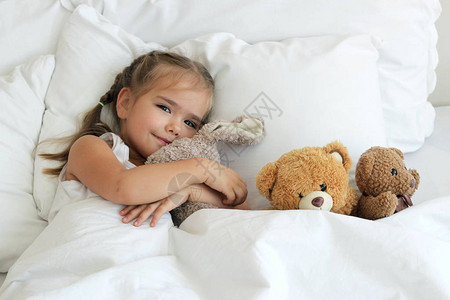 快乐可爱觉醒女孩的顶端风景带着玩具动物睡觉时间童年和家庭概念近图片