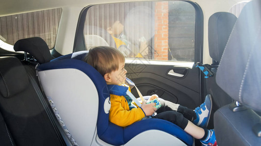 2岁小男孩坐在安全座椅上与玩具汽车一起图片