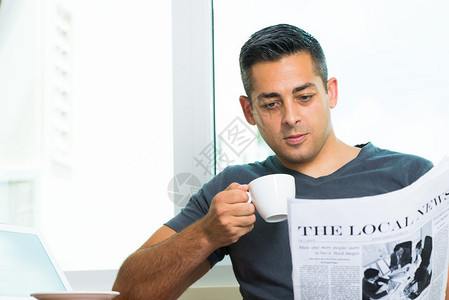 一名年轻人喝早咖啡和在家看报纸的影象复背景