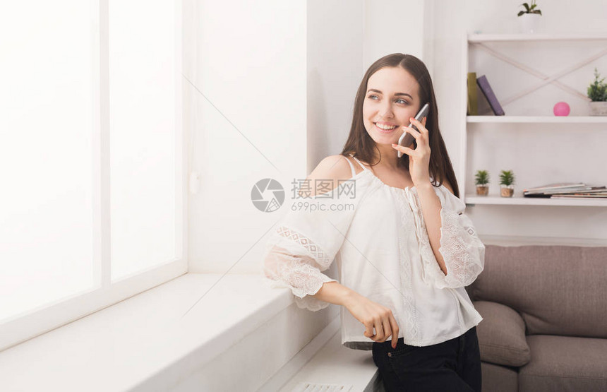 快乐的女士在手机上交谈站在窗户旁图片
