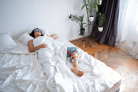 妇女睡在带白床单的白色墙房床上背景图片