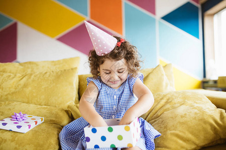 笑可爱的小女孩深卷发在生日帽子快乐地在家里沙图片