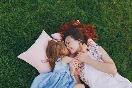 温柔的女人和可爱的小女孩躺在公园的草地上的枕头上拥抱拥抱和休息图片