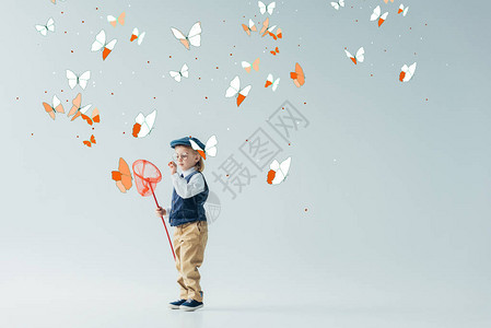 穿着复古背心和帽子的可爱金发小孩拿着灰色背景的蝴蝶图片