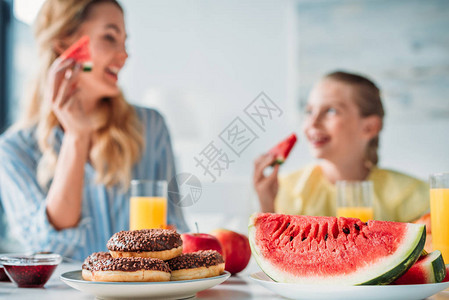 有选择聚焦镜头母亲和女儿与甜圈和西瓜共进早餐图片
