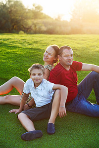 快乐的家庭和儿子坐在公园的草地图片