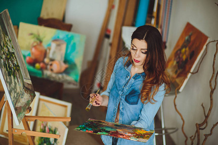 女艺术家在工作室里画一幅画创造沉思画家女孩在车间用油画颜料在画布上画出一幅五图片