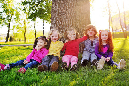 一群快乐的小孩微笑着坐在公园里一棵树下的草地上图片