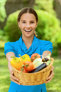身穿蓝色上衣带水果和蔬菜篮子的深色头发微笑着容的年轻女子肖像图片