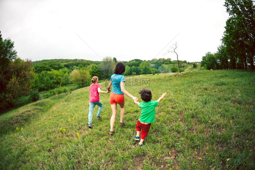一个带着孩子的女人沿着绿草奔跑妈牵着她的儿子们奔跑一个男孩和他的家人在户外玩耍孩子和他的母亲和兄弟图片