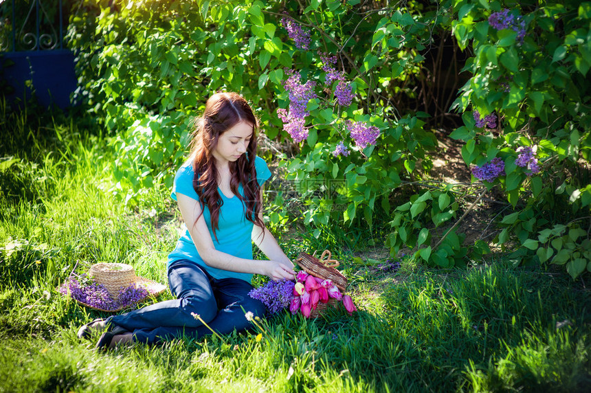 美丽的女孩坐在草地上春公园里有一束花朵图片