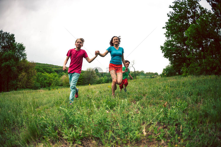 一个带着孩子的女人沿着绿草奔跑妈握着儿子的手笑着一个男孩和他的家人在户外玩耍孩子和他的母亲和兄弟图片
