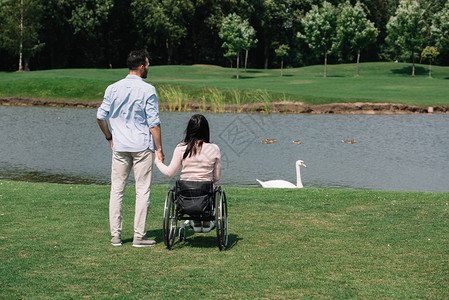 看着公园池塘时与残疾妇女的年轻男图片