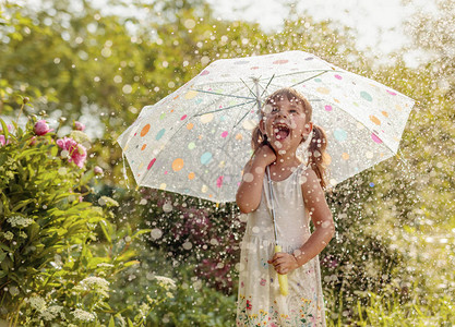 快乐的小女孩在夏雨下在花园里玩耍用伞图片