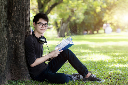 亚裔英俊男青年学生阅读自然本背景图片