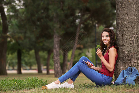 美丽的年轻女士在公园树旁听音图片