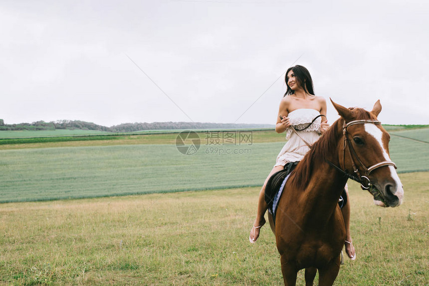 美丽的女人在田野上骑着棕色的马图片