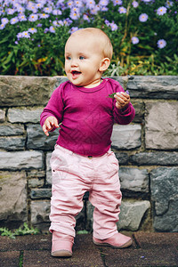 可爱的912个月大女婴玩紫色花朵穿着粉色裤子皮靴和紫色身图片