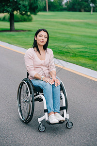 坐在轮椅上的年轻残疾青年妇女在公园中行走时图片