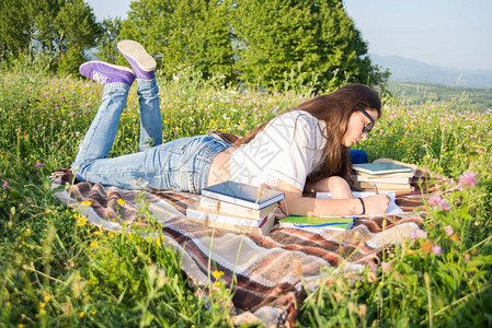 美丽的女孩躺在草地上在户外阅读和写书图片