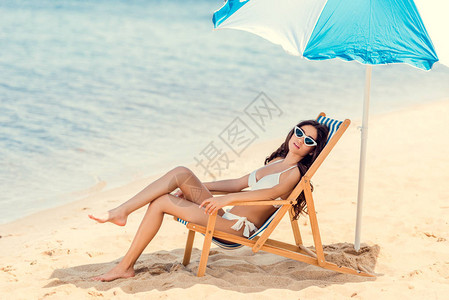 穿着太阳眼镜和比基尼的女人在海边雨伞下图片