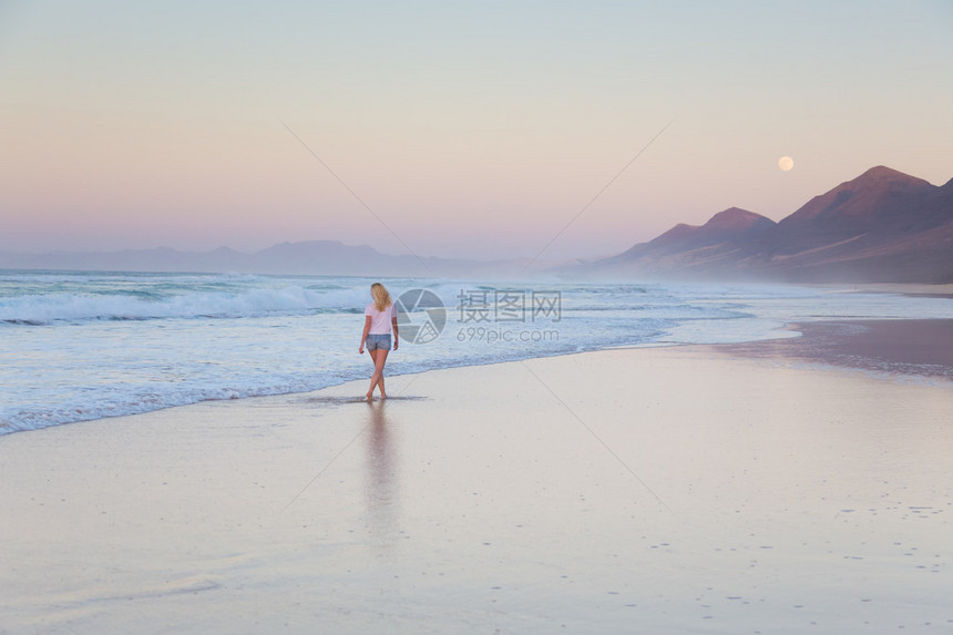 日落时分走在沙滩上的女人海浪扫去她在沙滩上的痕迹海滩图片