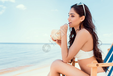 穿着比基尼的漂亮女孩在海滩上喝椰子鸡图片