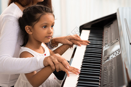 帮助她女儿弹钢琴弹体和扣子的妇女被数字图片