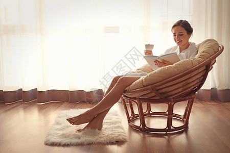 青年妇女在家里的休息椅上读书时喝咖啡图片