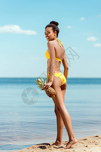 穿着比基尼的非洲裔美国女人在沙滩上拿着菠萝图片