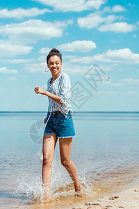 快乐的非洲女游客在沙滩附近的海水中行走图片