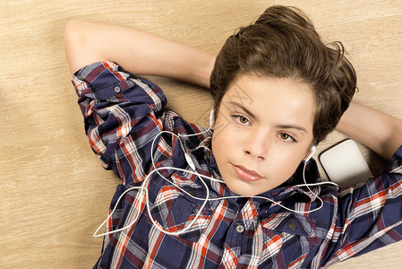 一名男孩在家中的木地板上用耳机拉伸着耳机听音乐图片