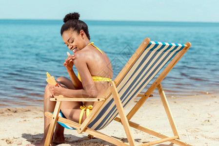 坐在沙滩的甲板椅上时在皮肤上涂防图片
