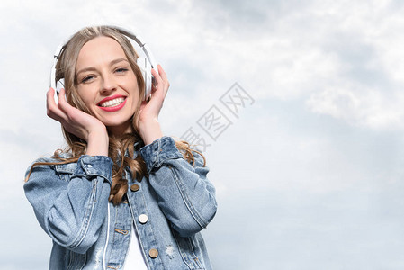 在天空下用耳机播放音乐的年轻微笑图片