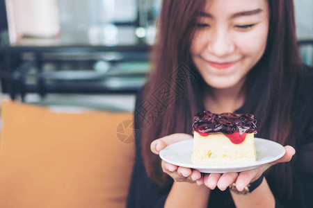 一个美丽的亚洲女人拿着蓝莓干酪蛋糕在现代咖啡馆里享受快乐和好生活方图片